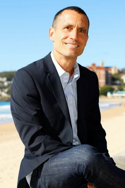 Max Dagenais, founder of Heart Safe Wellness, smiling on the beach in a navy blazer